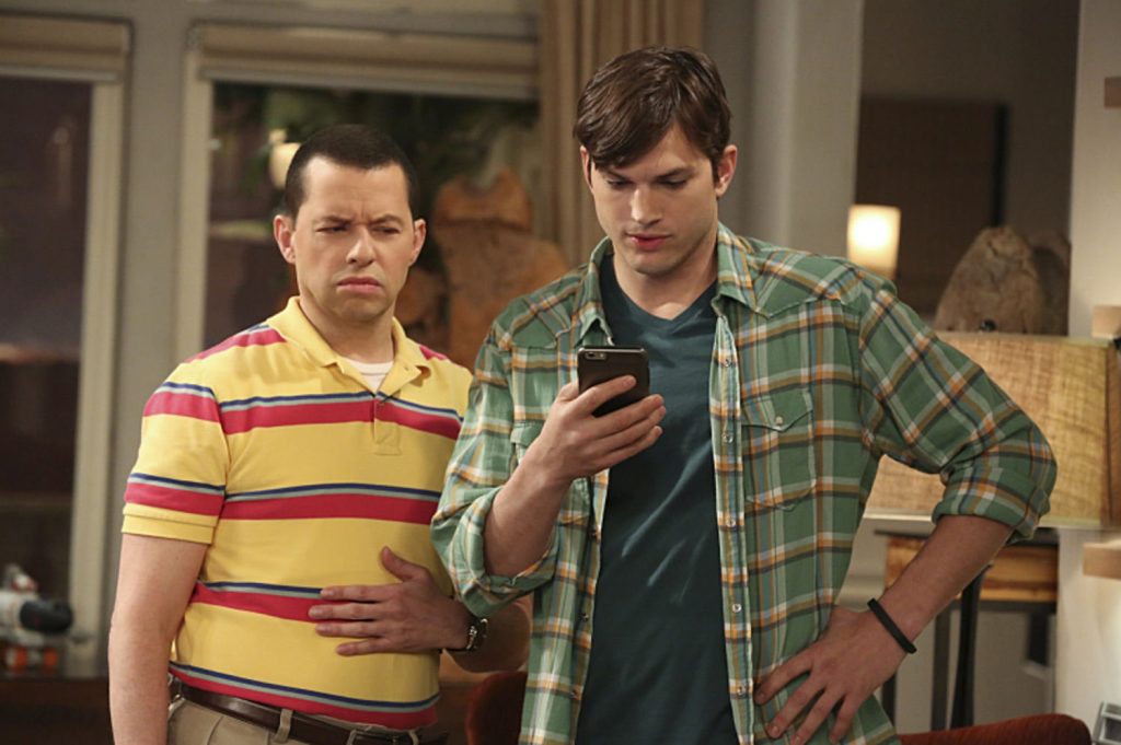 Alan (played by Jon Cryer) looking suspiciously at Walden's (played by Ashton Kutcher) phone, which he's holding in the series finale of "Two and a Half Men"